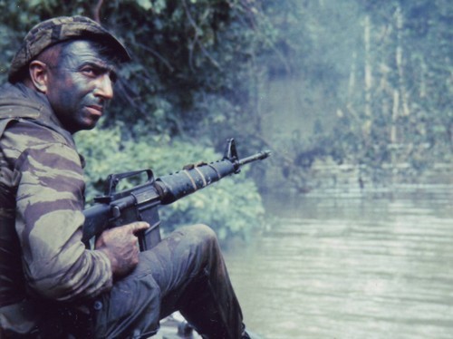 [SEALs] Petty Officer 1st Class and SEAL Team One member Sam Fournier wears grease paint as he keeps watch from a landing craft on the Bassac River. Photo taken: November 1967