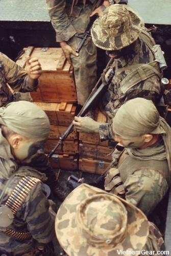 [SEALs] SEAL team members wearing a variety of camouflage clothing check their weapons as they prepare to conduct an operation from a riverine craft. Photo taken: October 1968